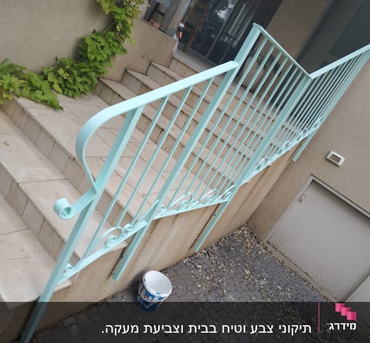 מעקה צבוע בצבע תכלת עם דלי צבע על הרצפה